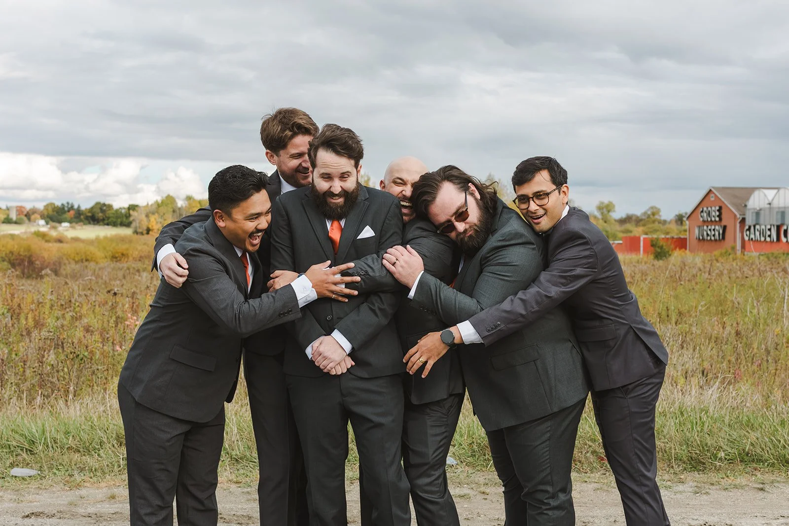 Groomsmen hugging groom on wedding day in a field  Cambridge Butterfly Conservatory  Cambridge, ON  Fedora Media.jpg