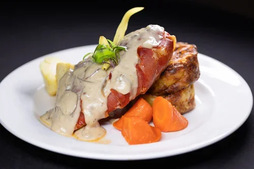 A plate with a meat dish topped with creamy mushroom sauce, accompanied by cooked carrots and a side of potatoes.