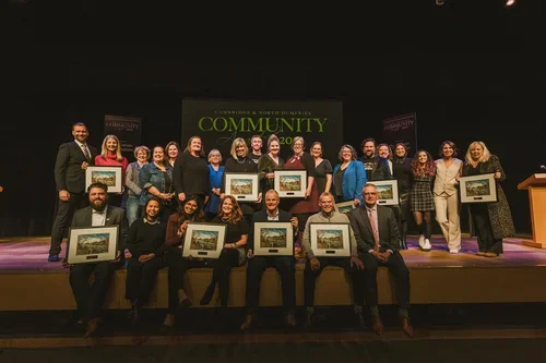 Group of people on stage holding framed certificates or awards, at a community recognition event.