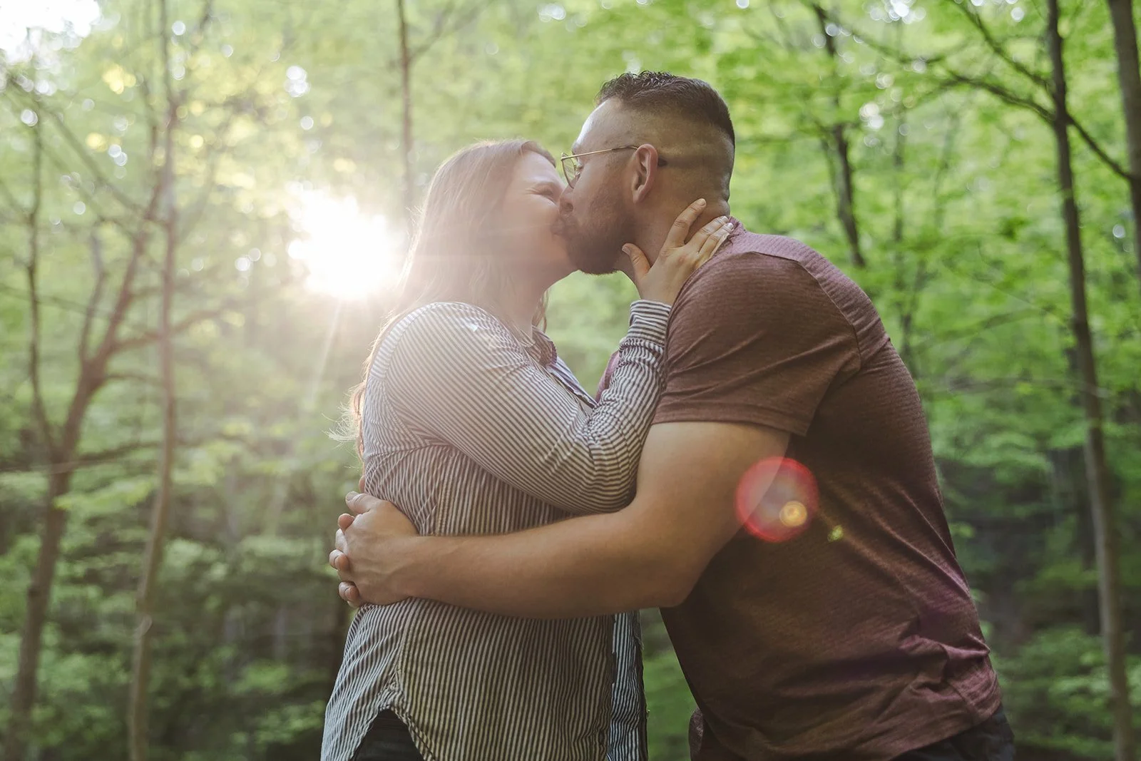 Couple kissing in forest with sun flair  Ontario Engagement  Fedora Media.jpg