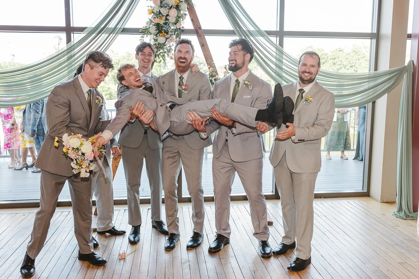 Groom holding bouquet being held up by groomsmen  River's Edge  Arlington Hotel  Paris, ON  Fedora Media.jpg