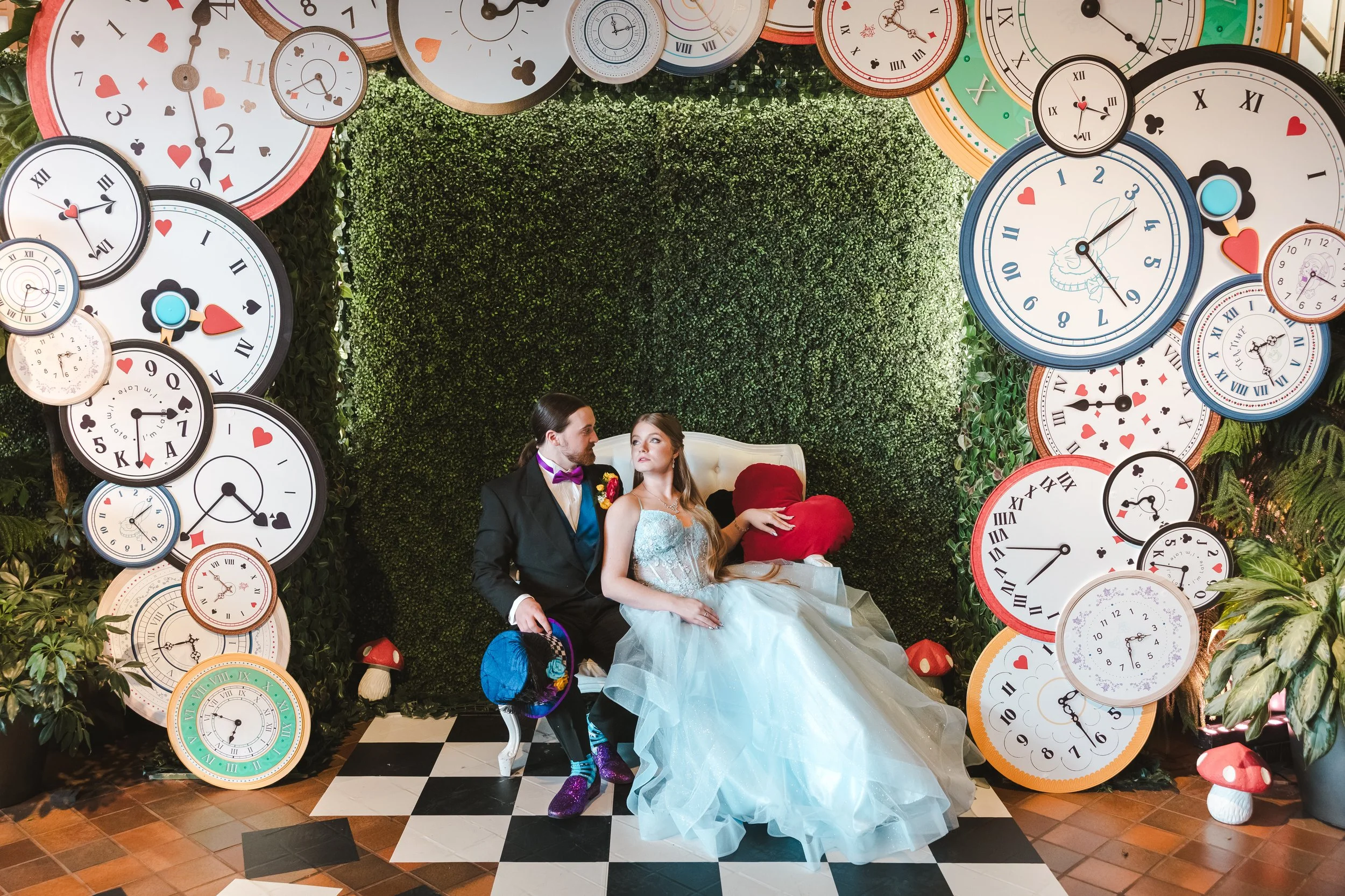bride-and-groom-sitting-on-chaise-surronded-by-clocks-alice-in-bloomland-fedora-media.jpg