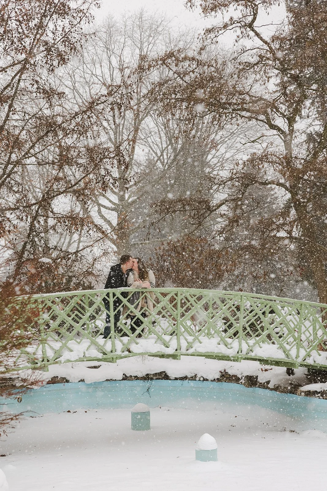 Couple kiss on bridge while it snows  Ontario Engagement  Fedora Media.jpg