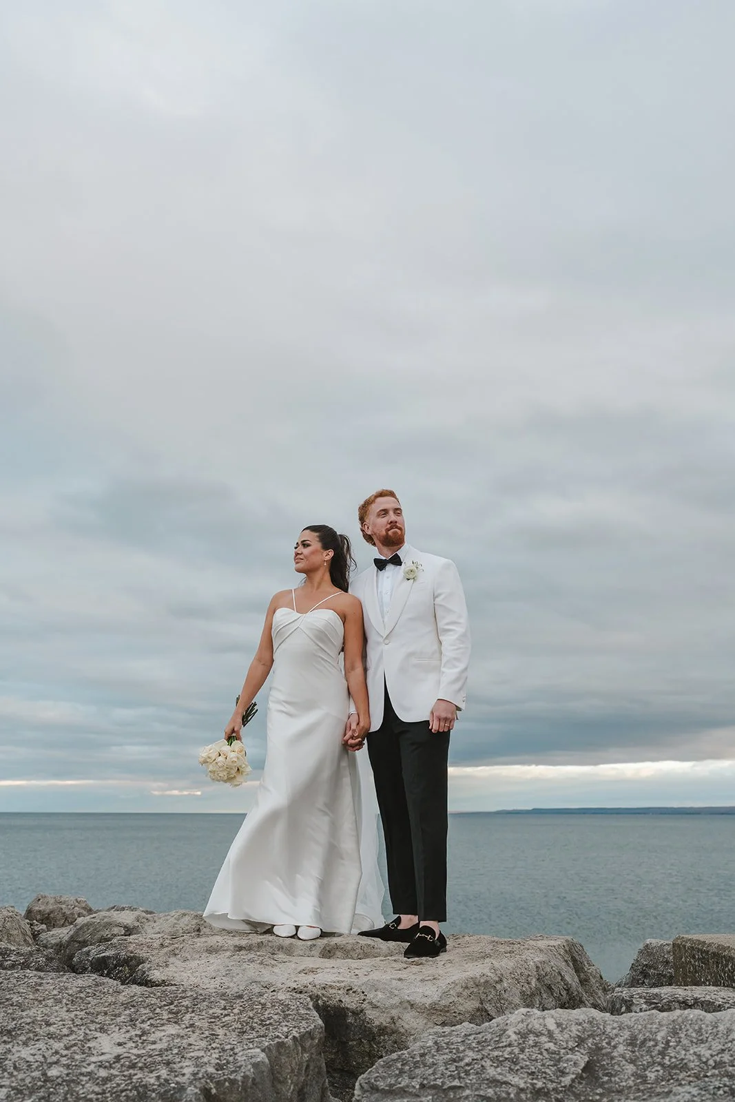 Bride and groom standing on rocks at edge of lake  Spencers at the waterfront  Pearle weddings  Burlington, ON  Fedora Media.jpg