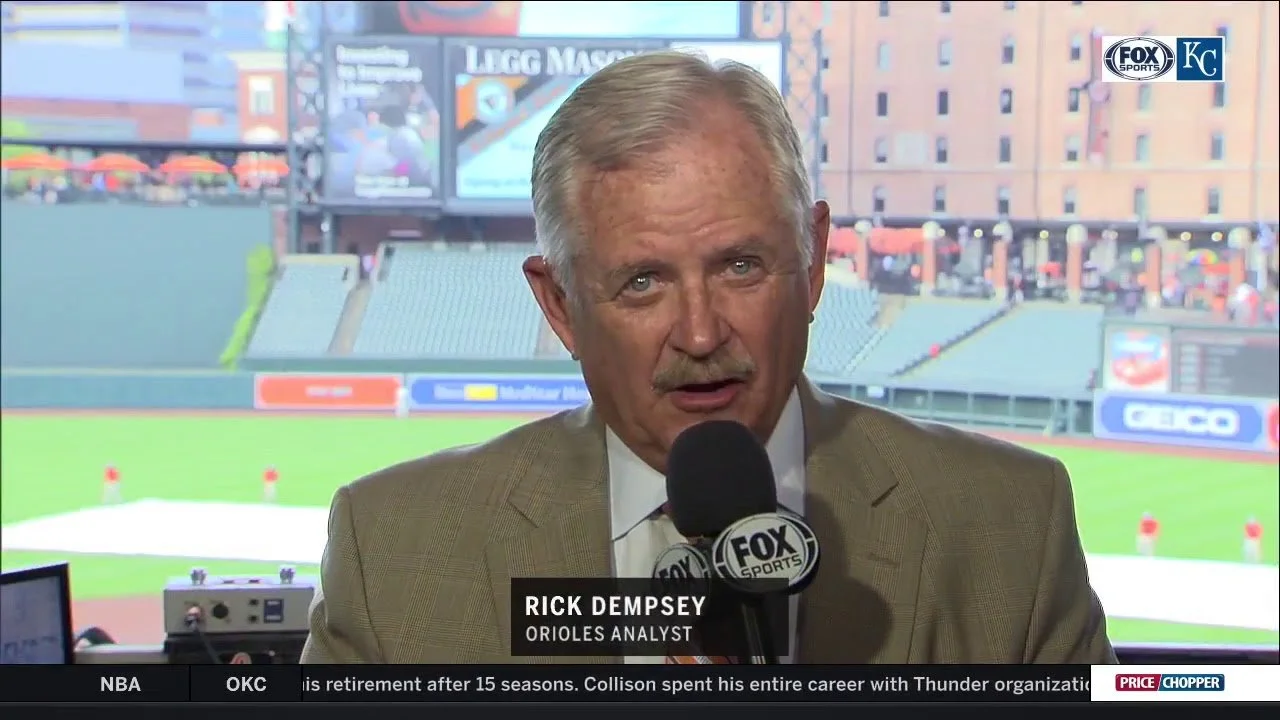 Rick Dempsey, Orioles analyst, speaking into a Fox Sports microphone with a baseball stadium background visible through the windows.