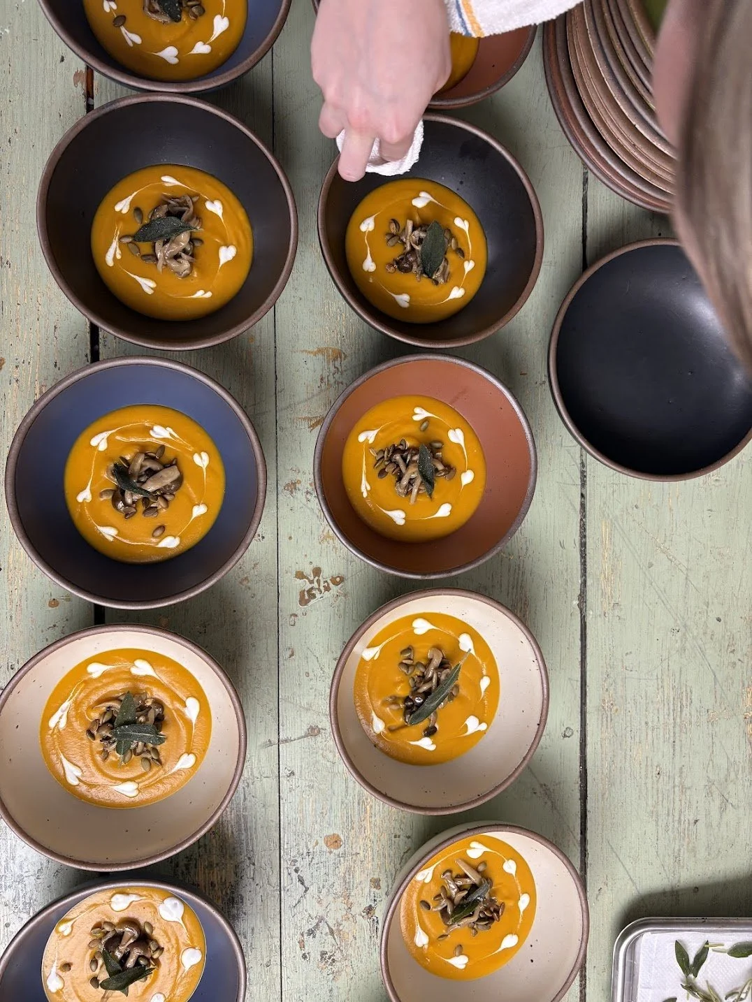 Top-down view of several bowls of pumpkin soup garnished with herbs and white sauce in a rustic kitchen setting.