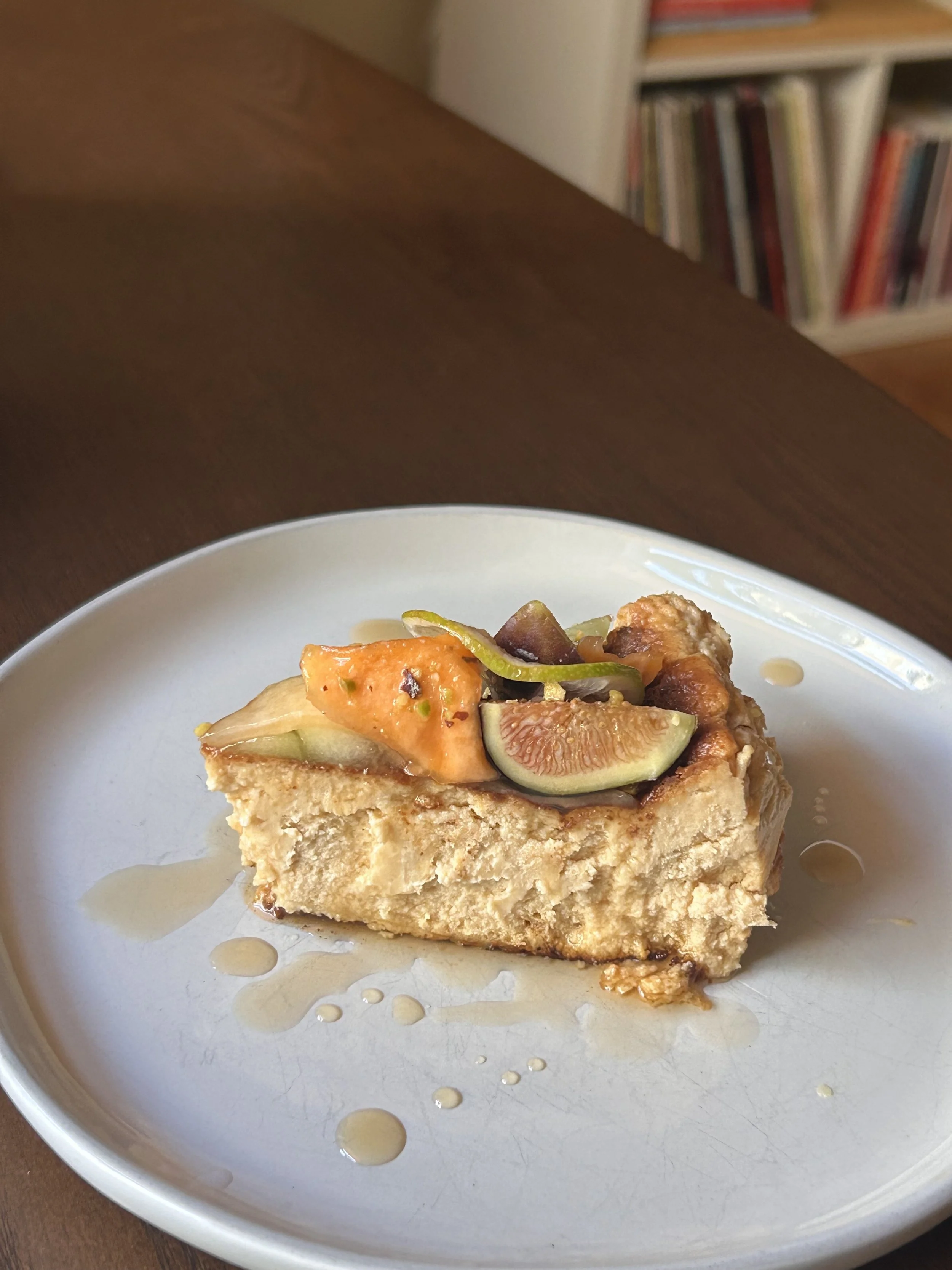 A slice of cheesecake topped with fresh figs, green grapes, and honey drizzle on a white plate.