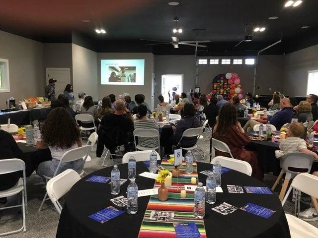 A large indoor event with attendees seated, listening to a speaker at the front of the room.
