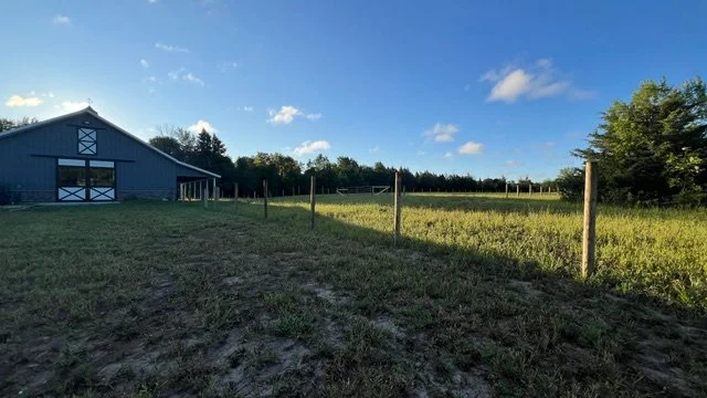A rural scene with a large blue barn, a grassy field, and a clear blue sky with some clouds.