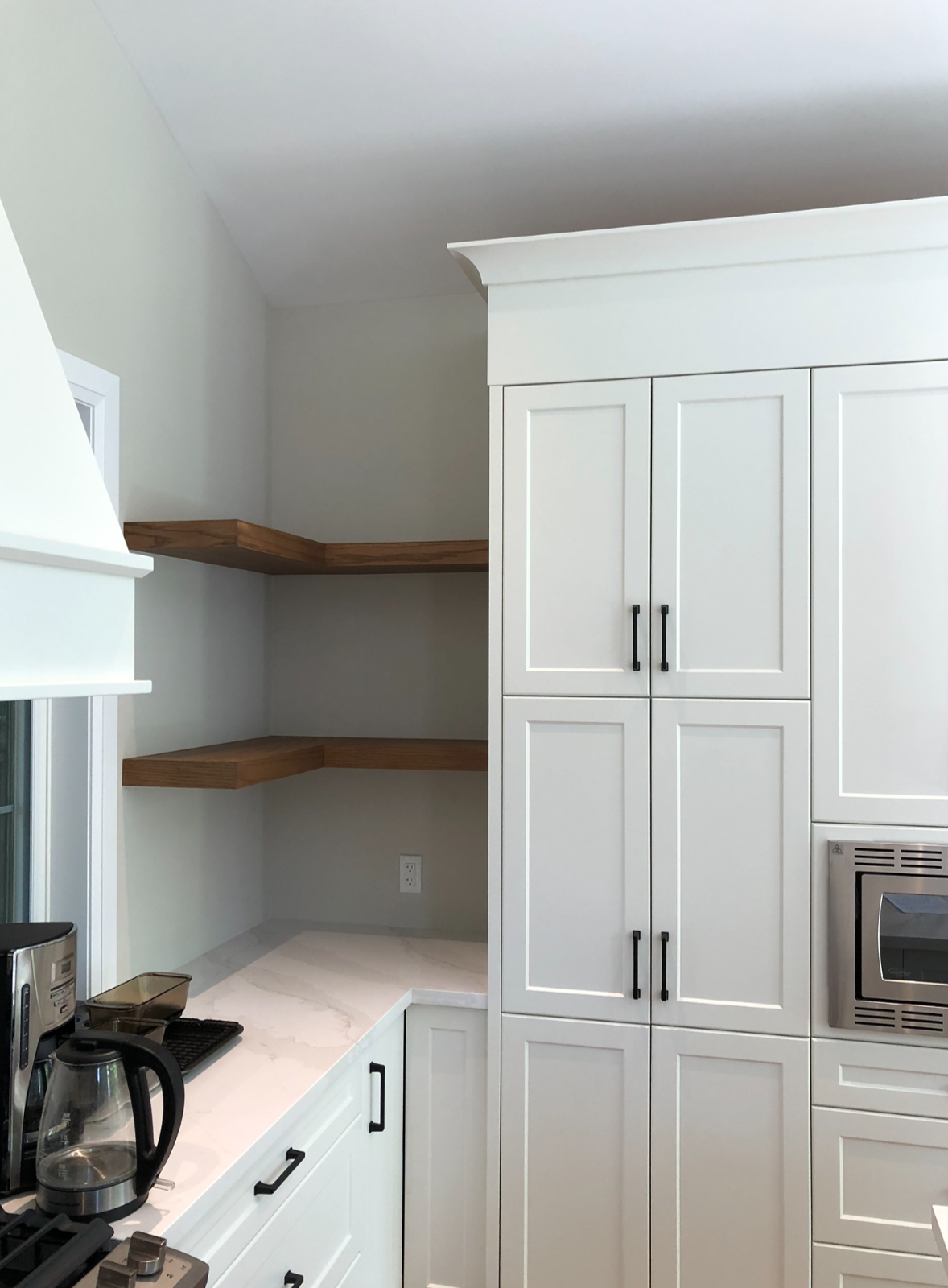 Kitchen with white cabinets, black handles, a microwave, and wooden open shelves on the wall.