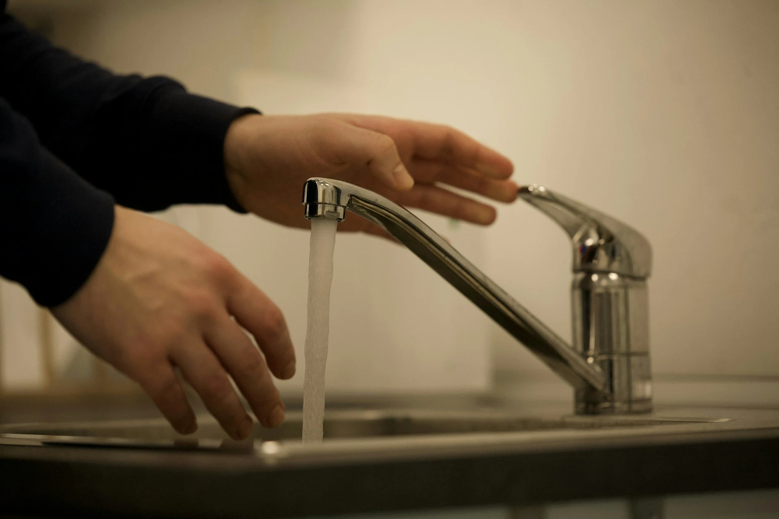 Person washing hands under running water from a kitchen sink faucet.
