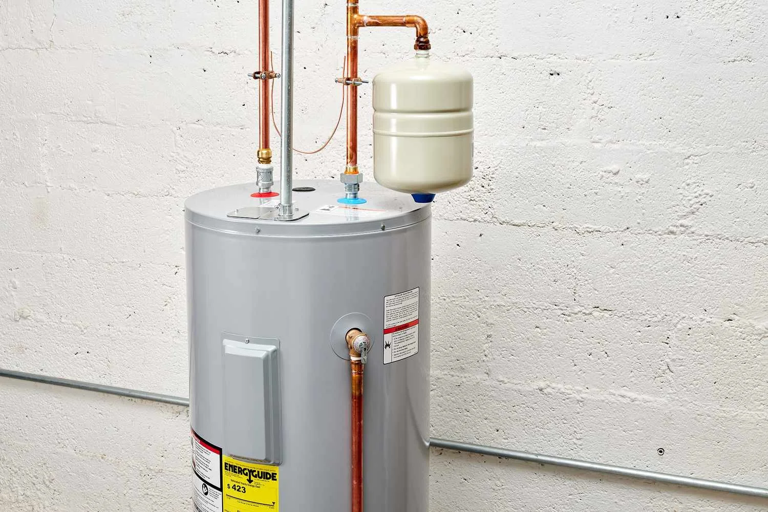 A water heater with copper pipes, a pressure relief valve, and an expansion tank mounted on a white wall.