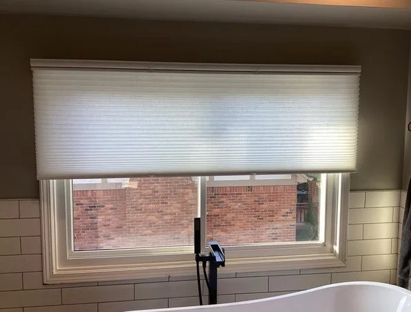 A window with a partially open white roller blind inside a room with white tiled walls.