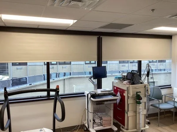 Medical office room with equipment, monitors, and chairs near windows with blinds