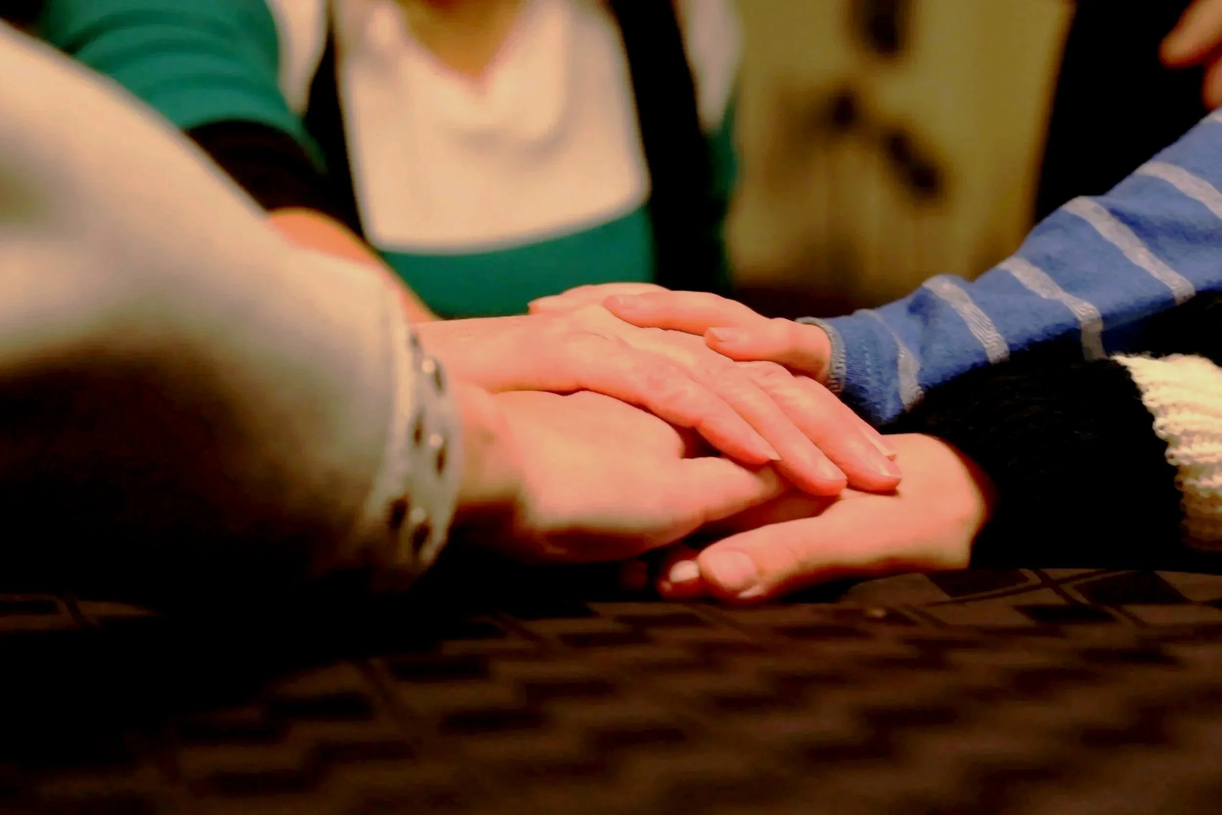 Multiple people placing their hands together in a show of unity over a dark, patterned table.