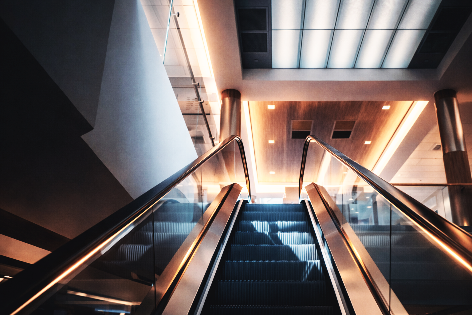 Escalera eléctrica en un interior moderno con techos de madera y iluminación cálida.