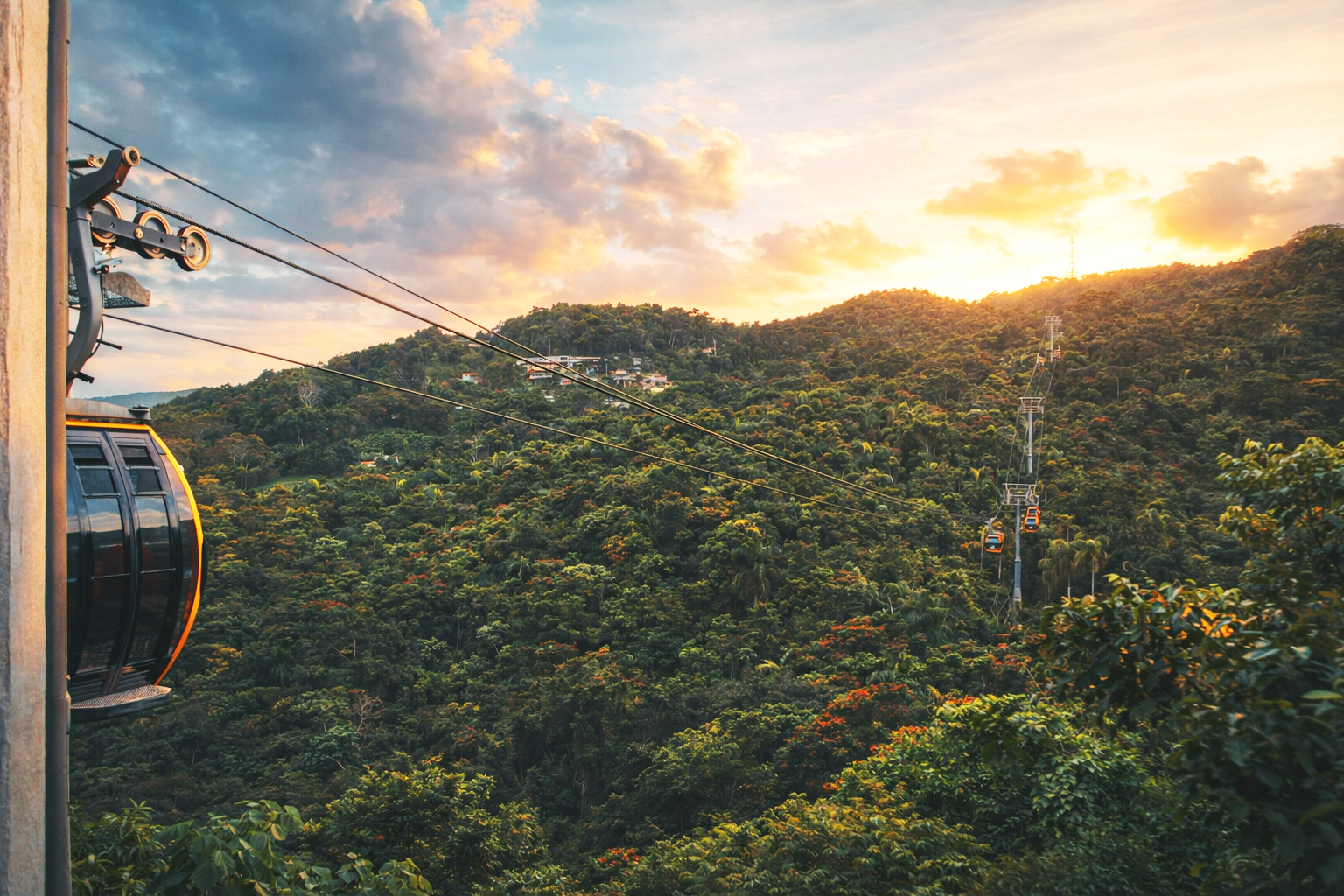 Vista de un teleférico sobre una selva al atardecer con nubes y un cielo con tonos anaranjados.