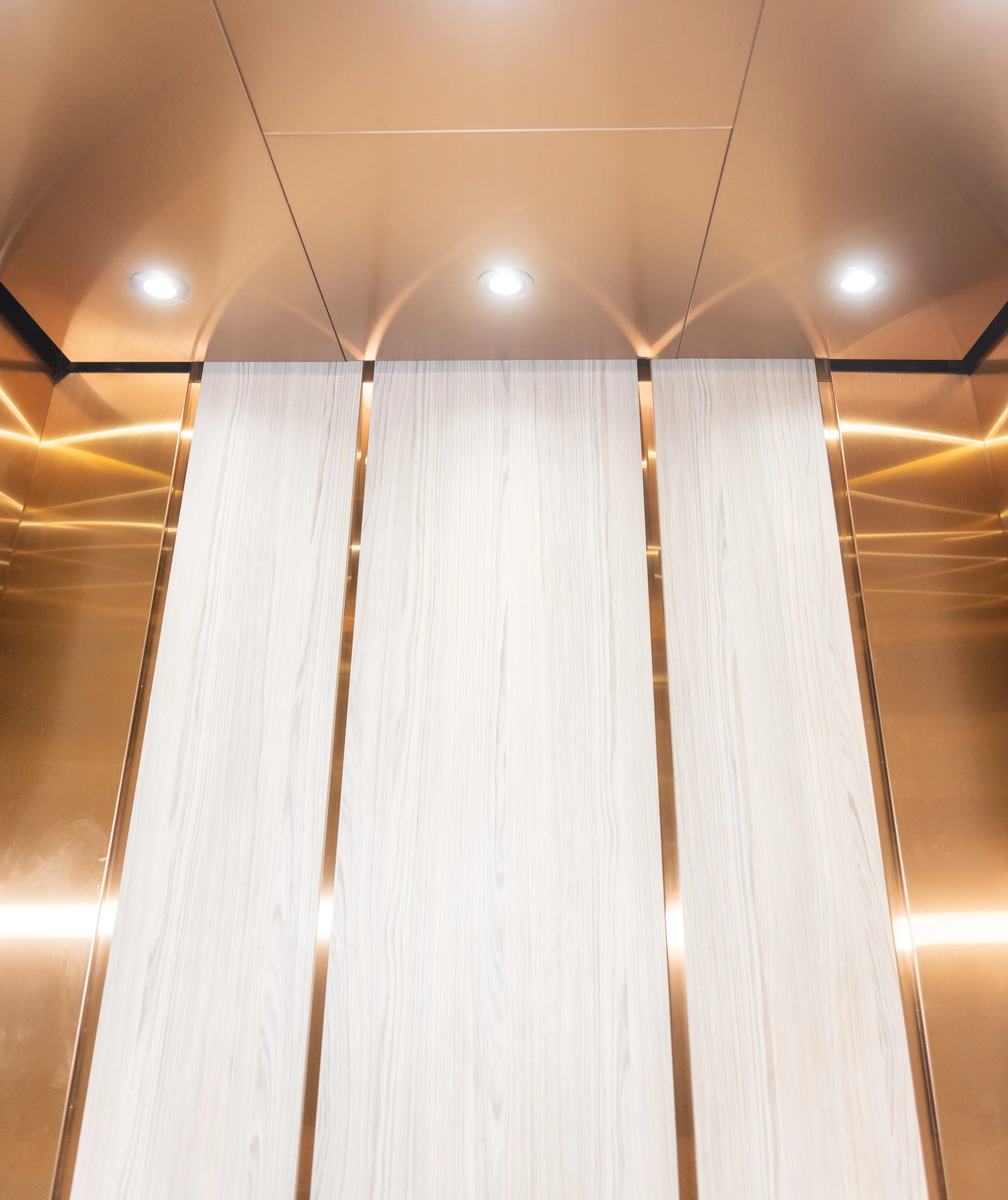 Puertas de un elevador con paredes doradas y luces en el techo.