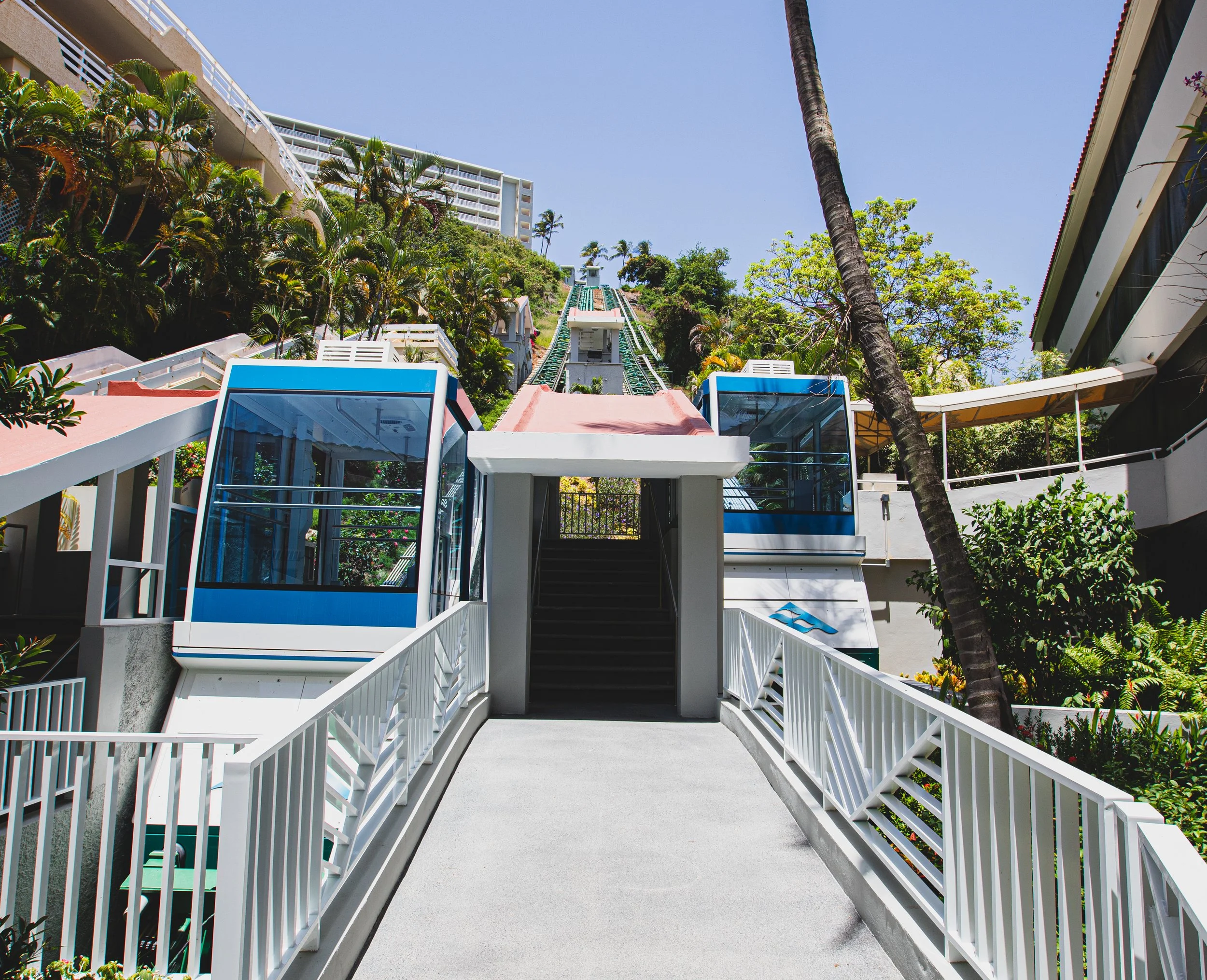 Estructura de un funicular en una zona montañosa con jardines y edificios en fondo, bajo un cielo despejado.