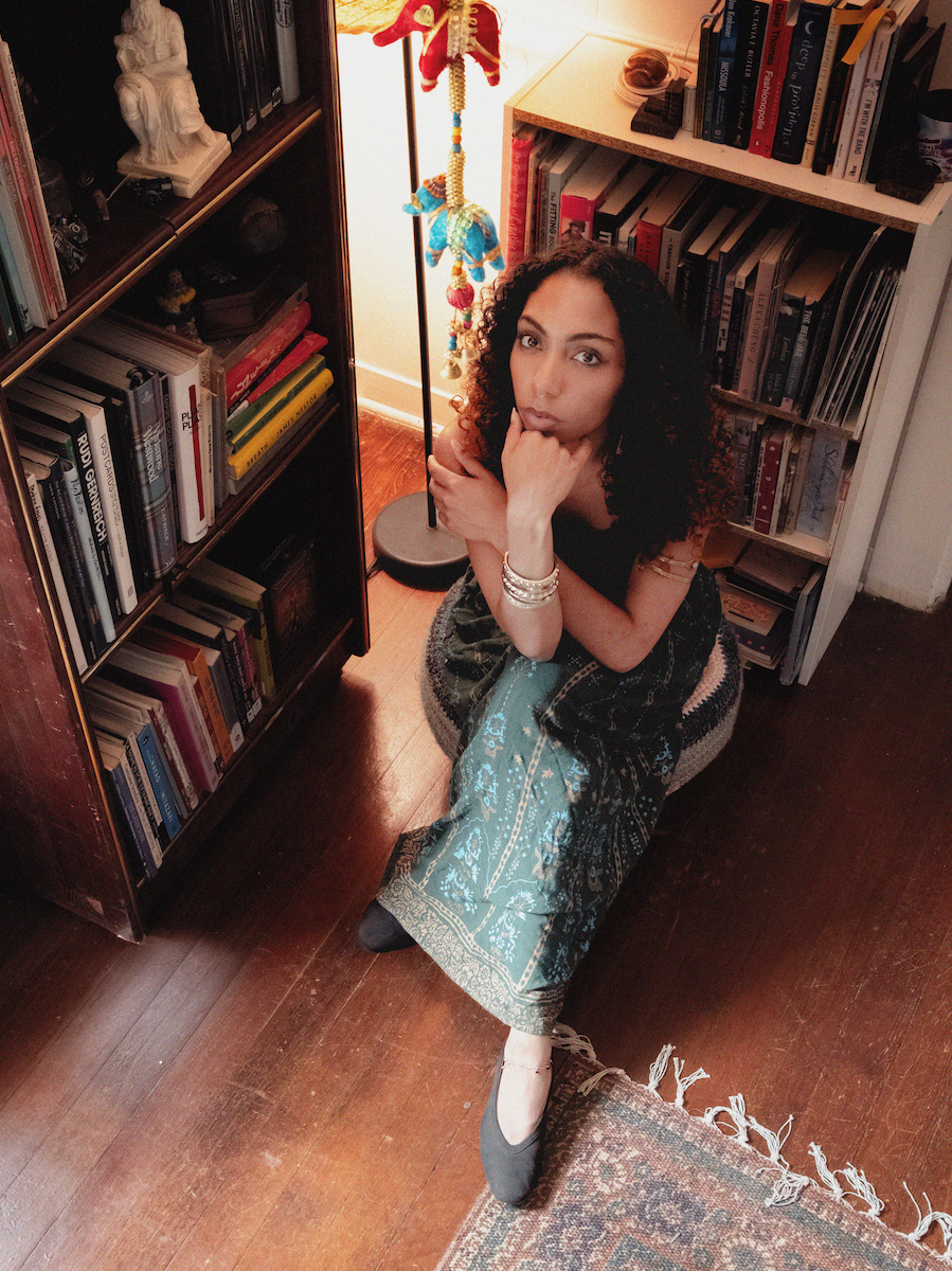 Chris Smith posing like The Thinker by Auguste Rodin by some bookshelves | Denton's premiere cosmic country band. 'Cosmic American Music' available on all streaming platforms. LPs/CDs. Flying since 2024!