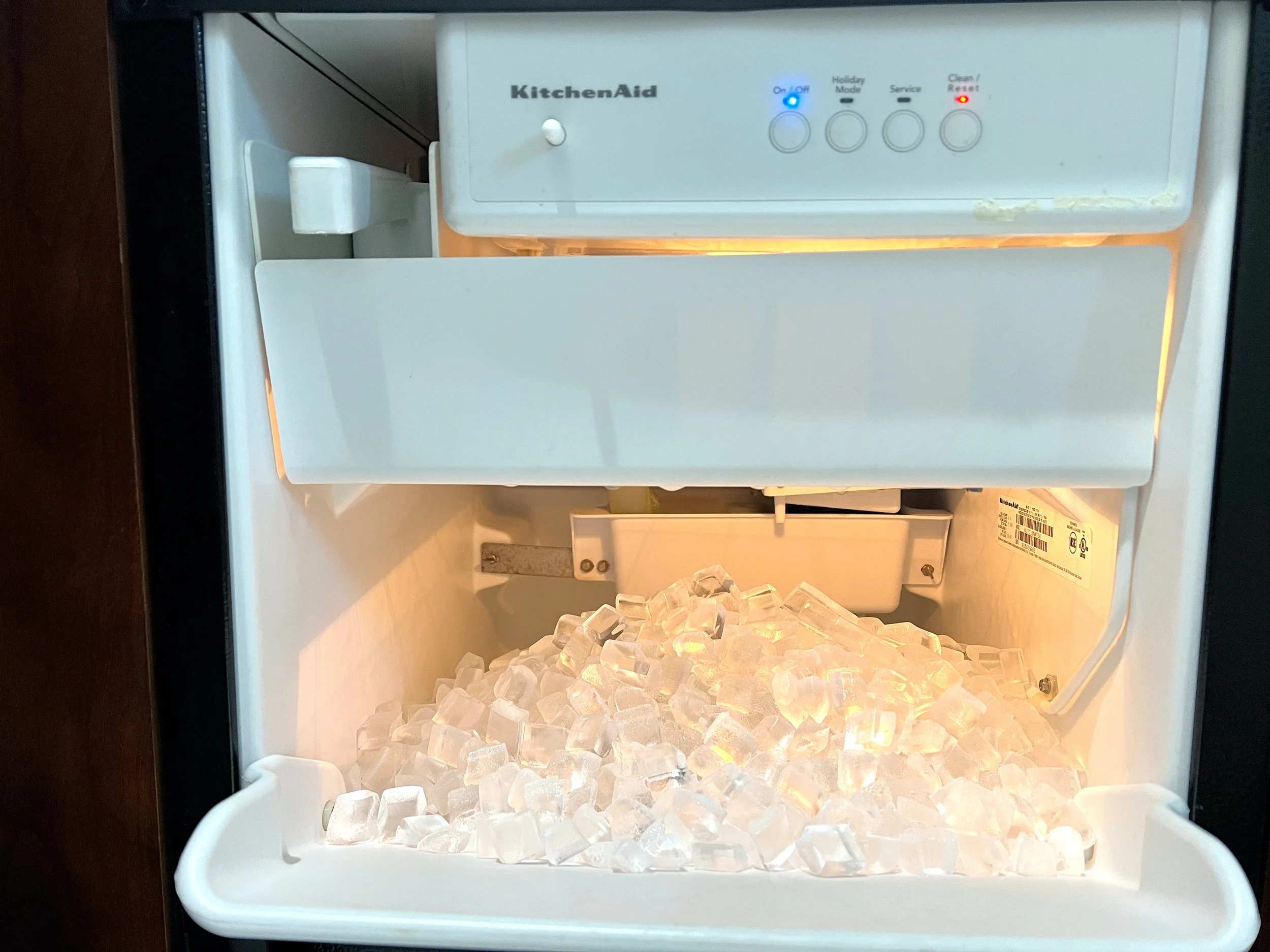 An open ice maker with a load of ice cubes inside, equipped with control buttons and indicators on the front panel.