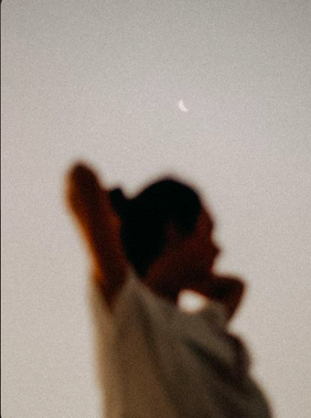 Blurred silhouette of a person with a hand behind their head, with a crescent moon in the sky above.