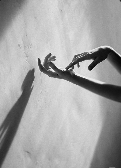 A person’s hand touching a wall with a shadow cast on the wall, in black and white.