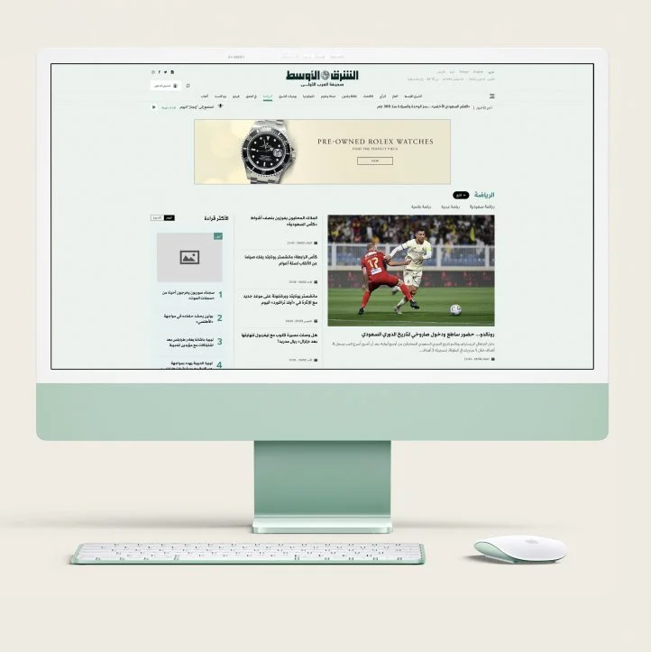 Computer monitor displaying a sports news website in Arabic, featuring a soccer match and an advertisement for pre-owned Rolex watches.