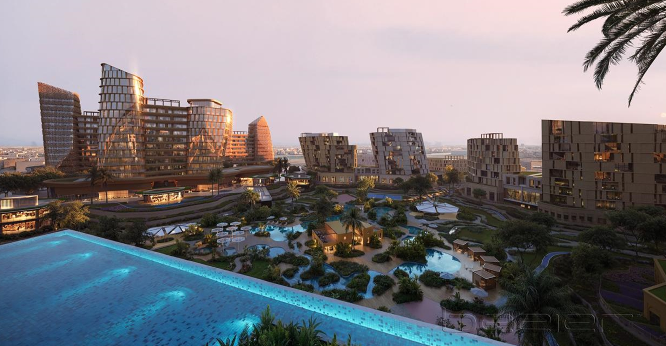 Aerial view of a modern resort with high-rise buildings, pools, and landscaped gardens at sunset.