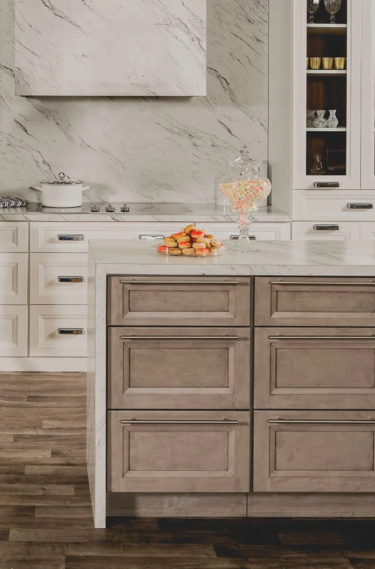 A modern kitchen with white cabinetry and marble countertops. There is a plate of cookies and a jar of marshmallows on the island counter.