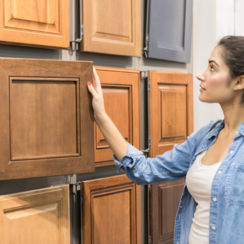 A woman examining wooden cabinet doors in a home improvement store.