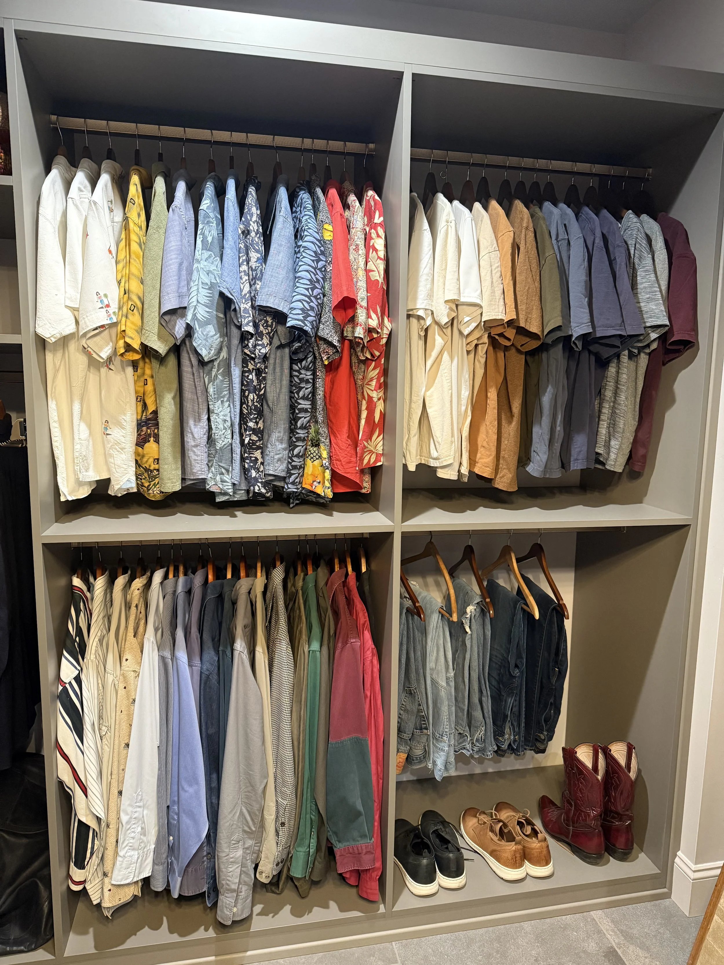 A closet with four sections of hanging shirts, shorts, and shoes, organized by color and style.