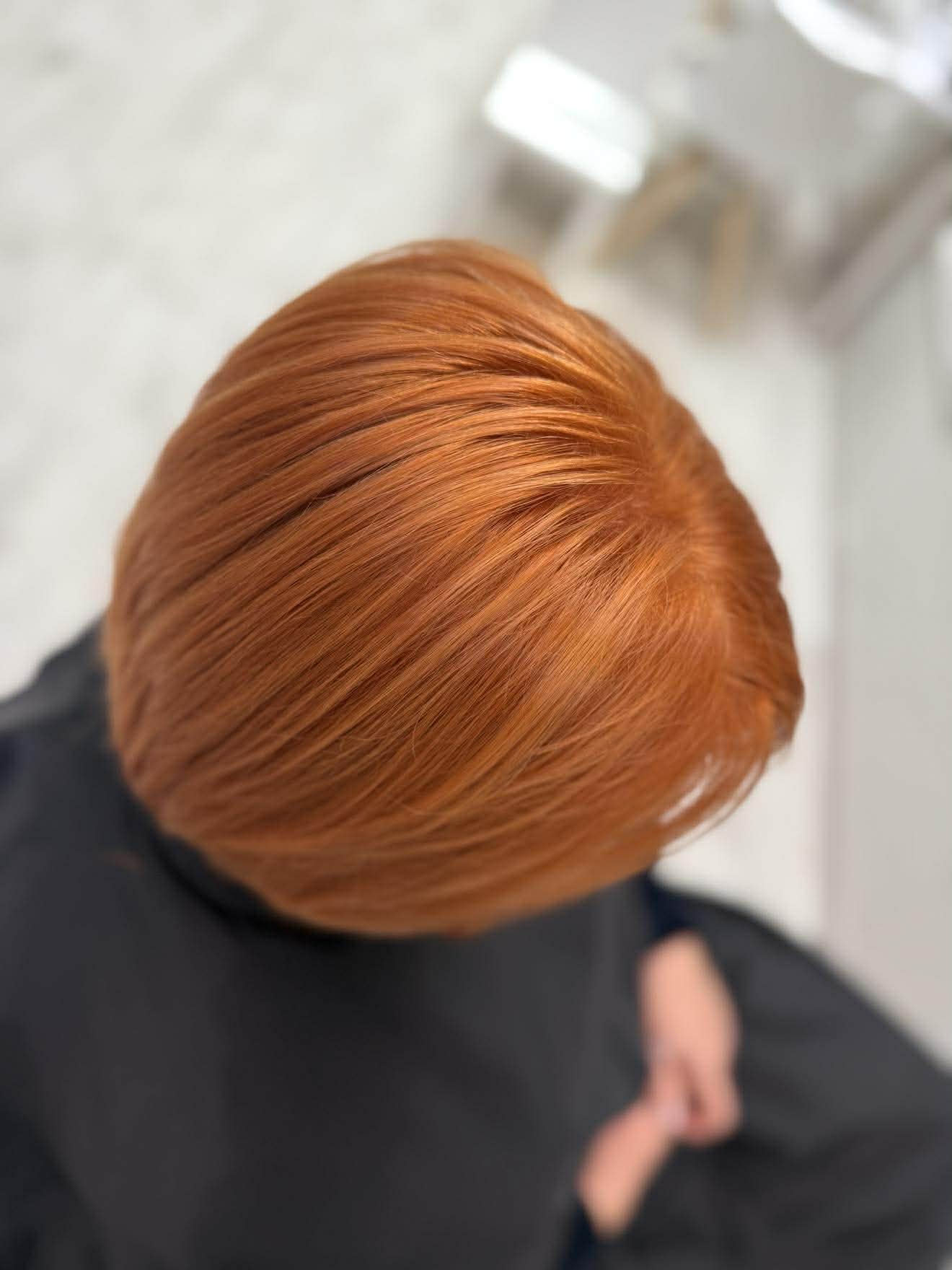 Lygiai sušukuoti, žvilgantys, ryškiai oranžiniai plaukai iš viršaus.