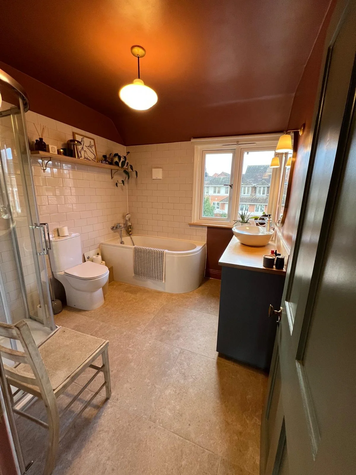 A bathroom with a bathtub, toilet, shower enclosure, window, vanity with a sink, and wall-mounted lights.