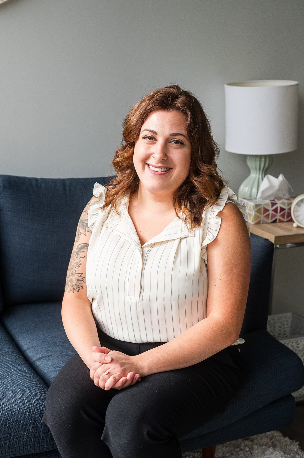 Diana Allura, founder of Allura, a sex-positive and trauma-informed sex therapy collective in Vancouver and Calgary. Diana is sat on a blue couch with a welcoming smile