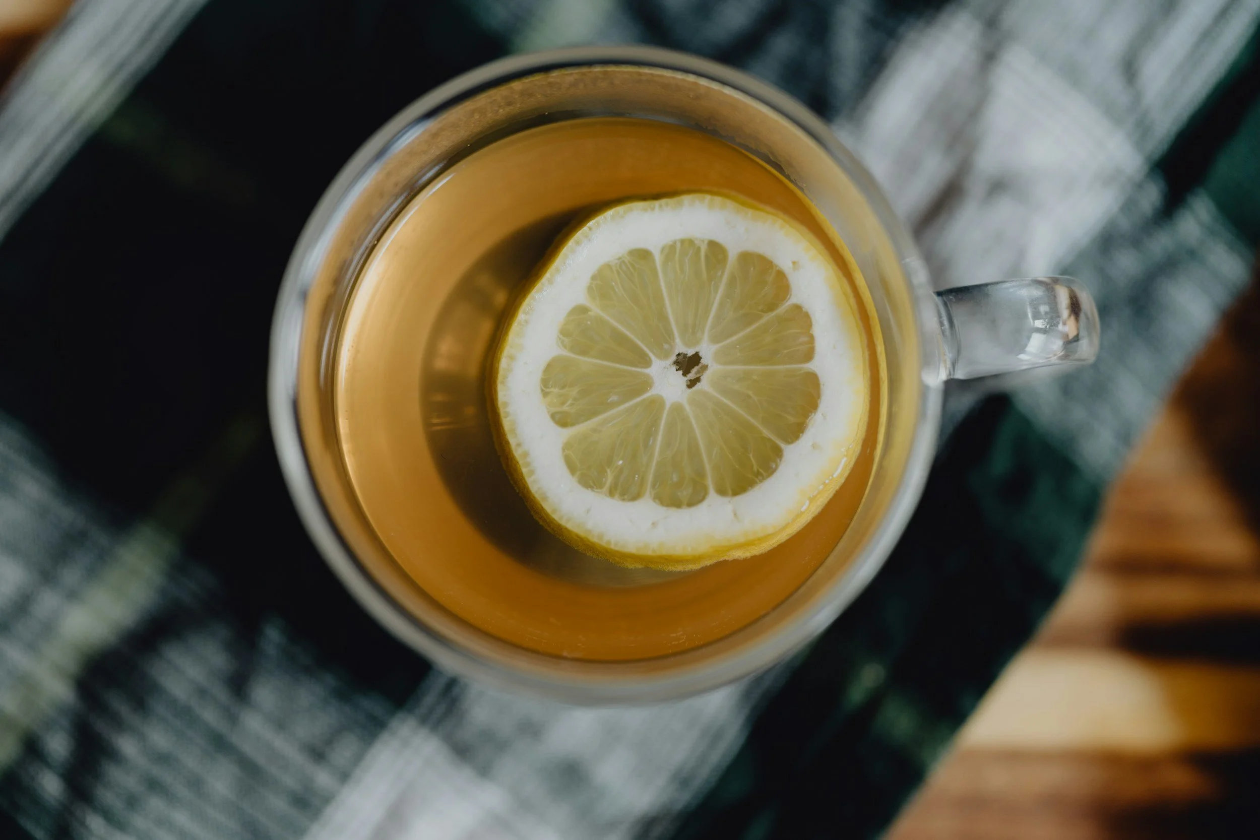 Glass mug of hot lemon tea on a cozy plaid surface at The Soul Space Wellness Café + Shoppe in Panama City, Florida, reflecting soothing wellness drinks.