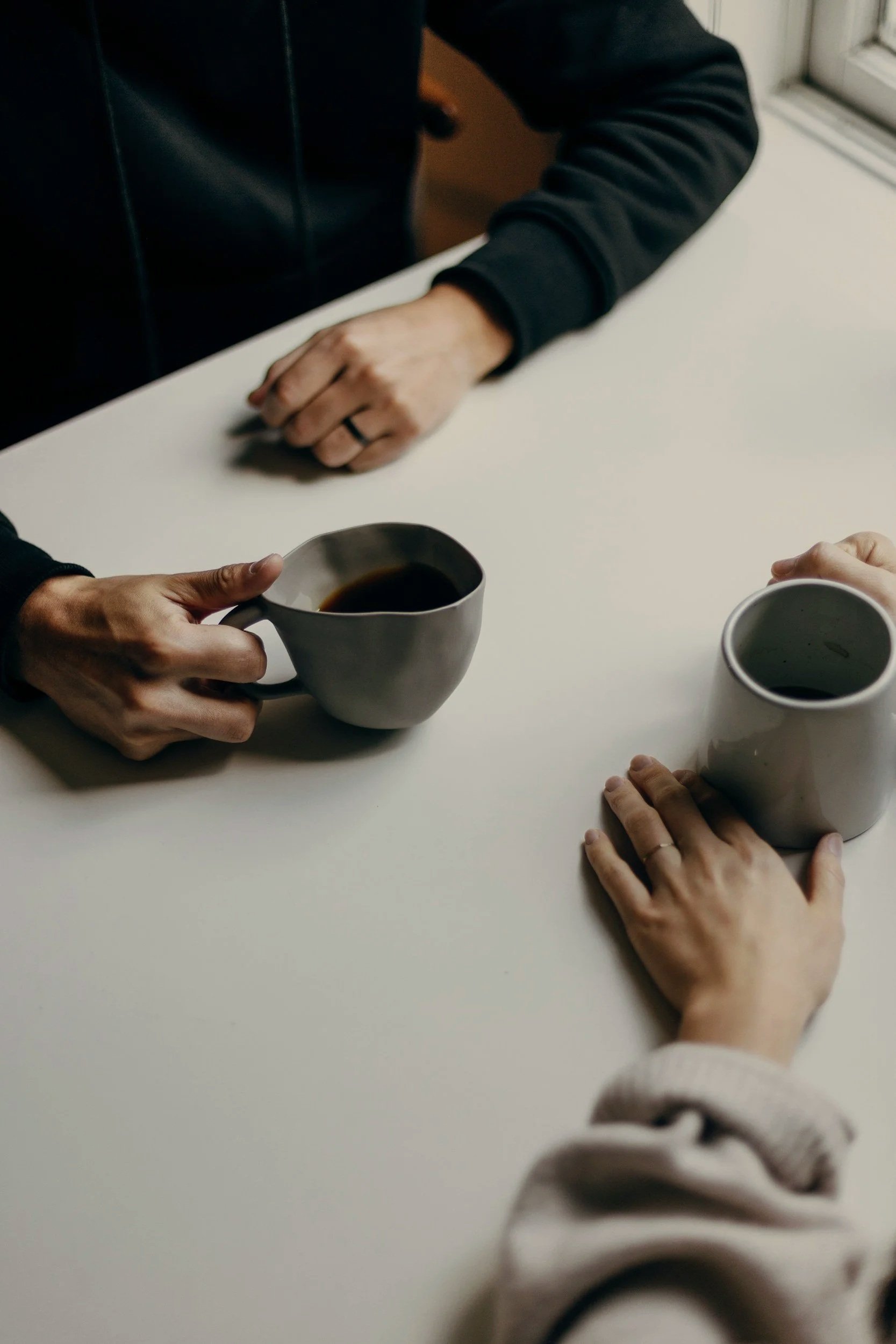 Two people sharing coffee across a minimal white table, symbolizing connection and community at The Soul Space Wellness Café + Shoppe in Panama City, Florida.