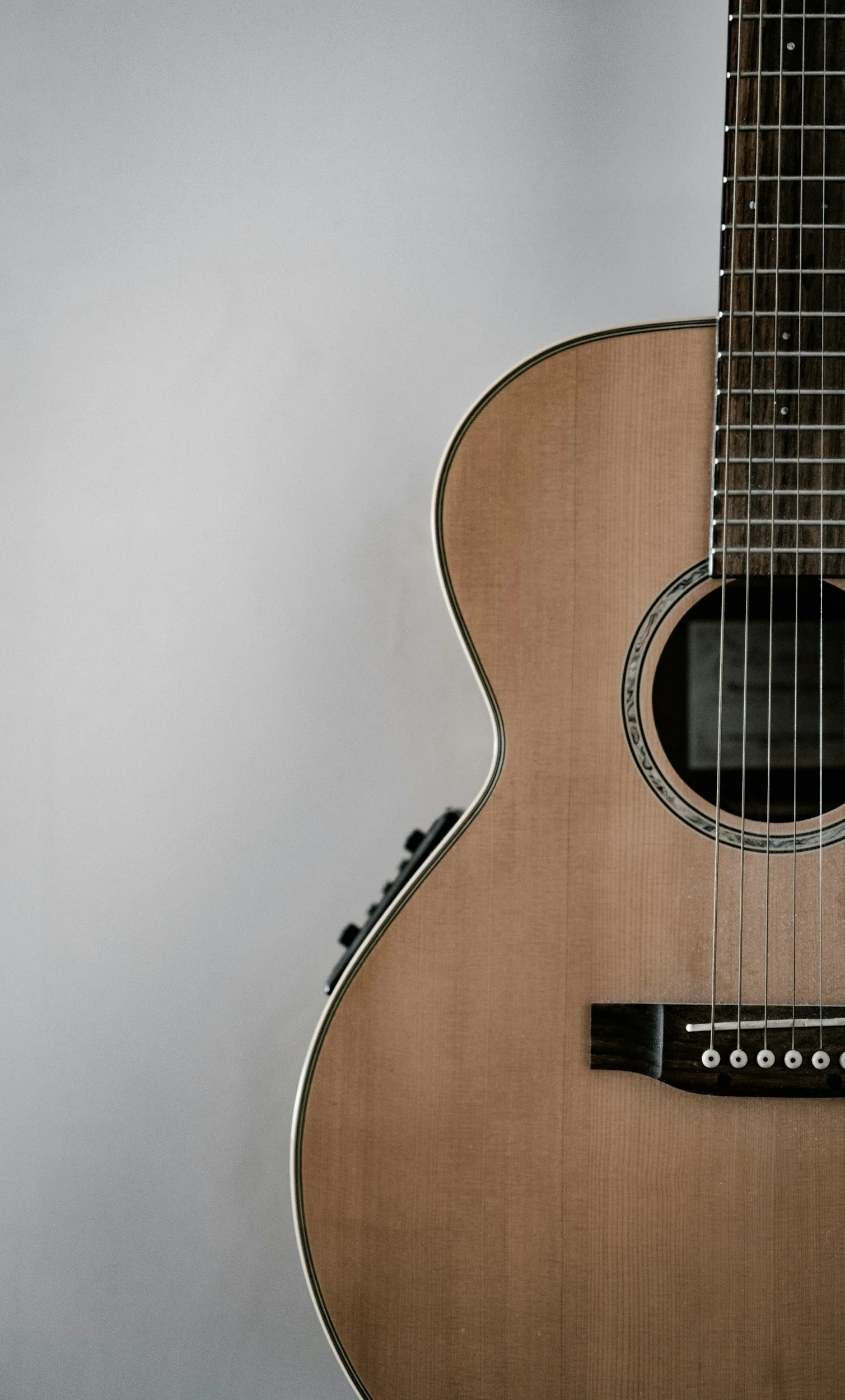 Close-up of an acoustic guitar showing part of the body, strings, and fretboard against a plain background.