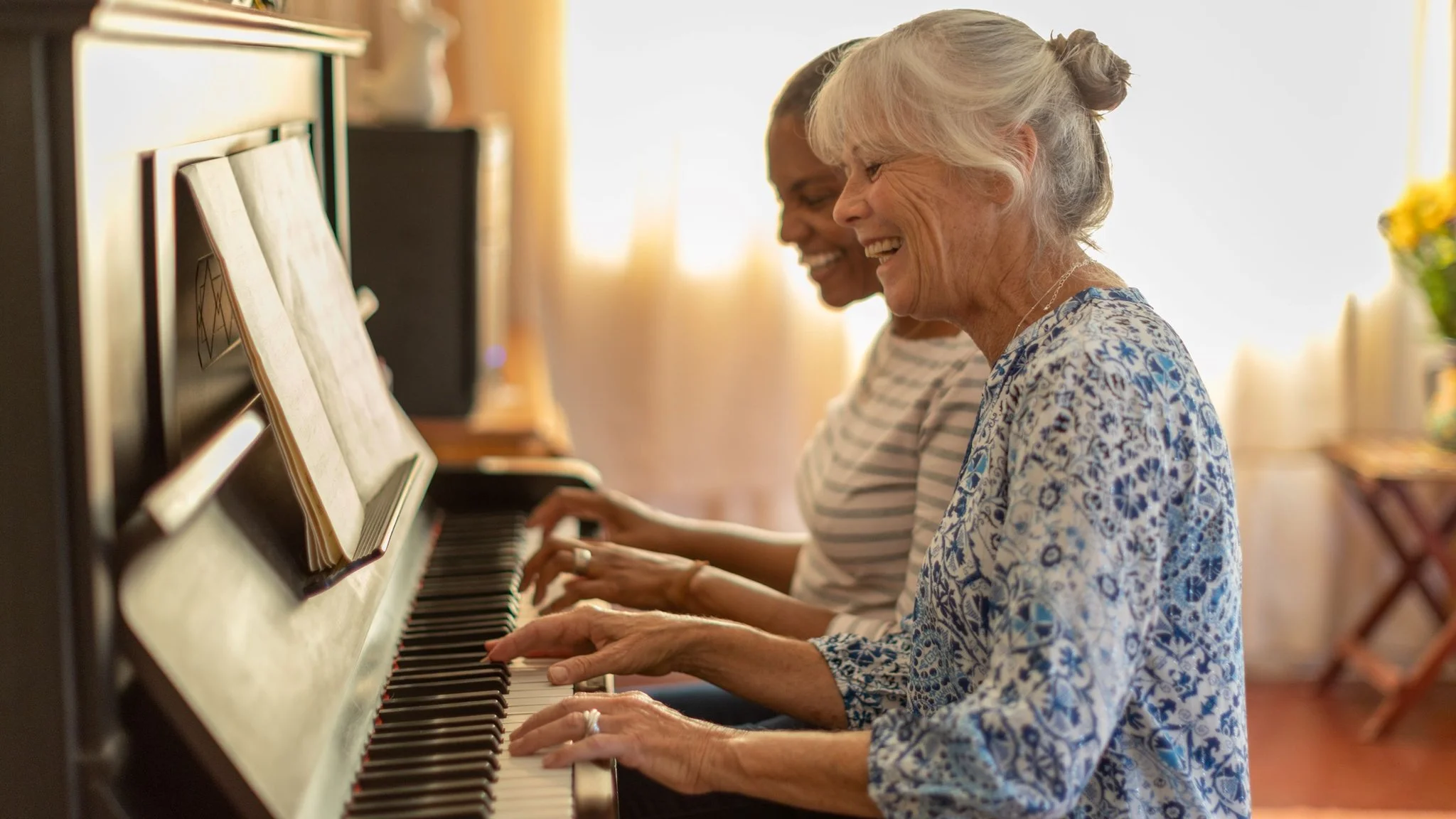 Two elderly women playing the piano together, smiling and enjoying their time.