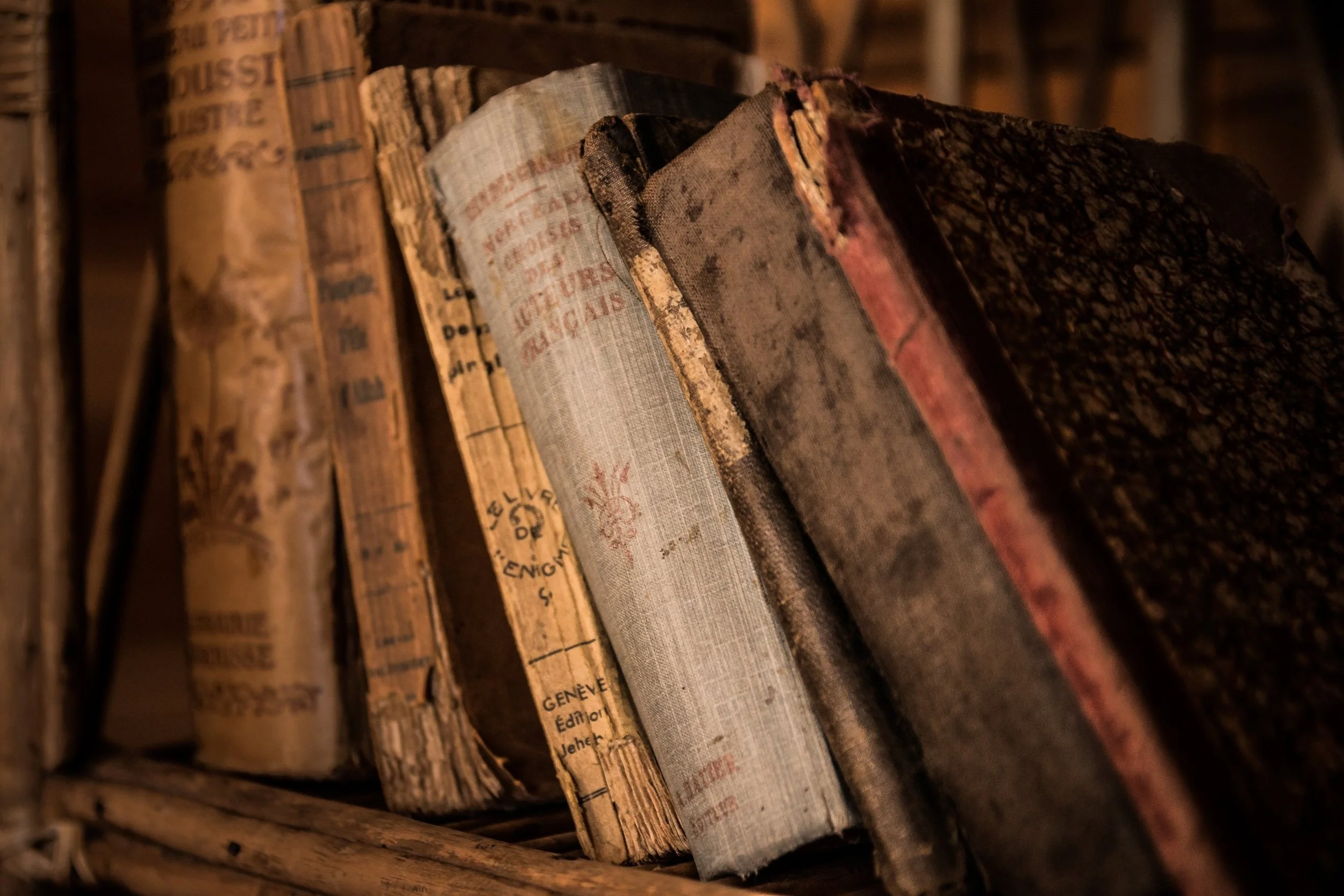 Close-up of old, weathered books with worn covers, stacked on a wooden shelf.