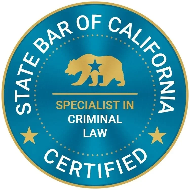 Seal or badge with blue background and gold border, featuring a gold bear with a star on its side, and text indicating certification as a specialist in criminal law from the State Bar of California.