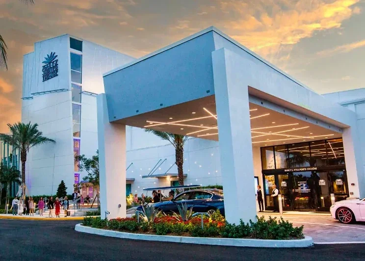 Exterior view of the Shops at Summerlin shopping center during sunset, with modern white building, palm trees, parked cars, and people walking.
