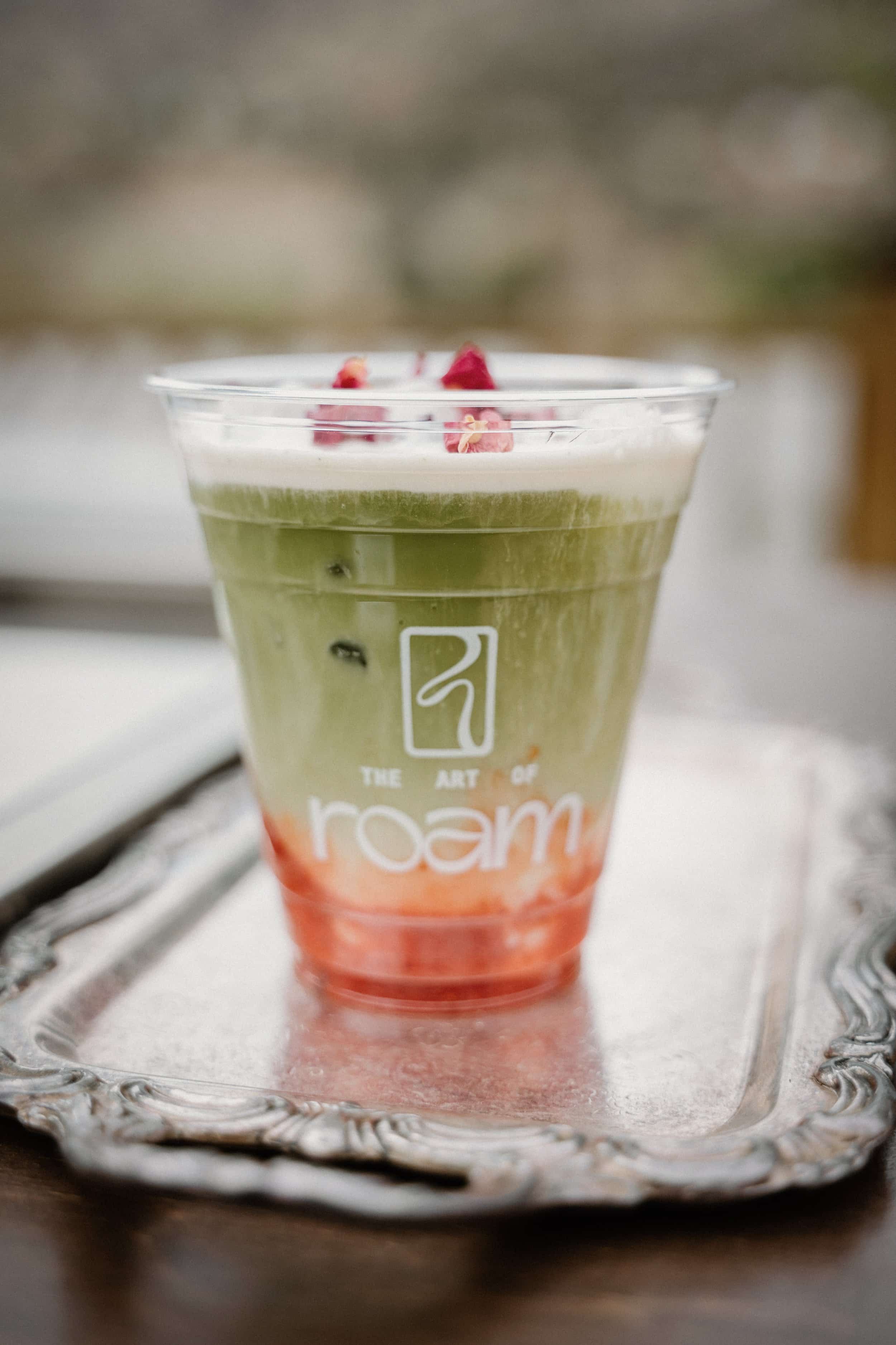 Iced strawberry matcha latte layered with milk and fruit purée in a branded The Art of Roam cup.