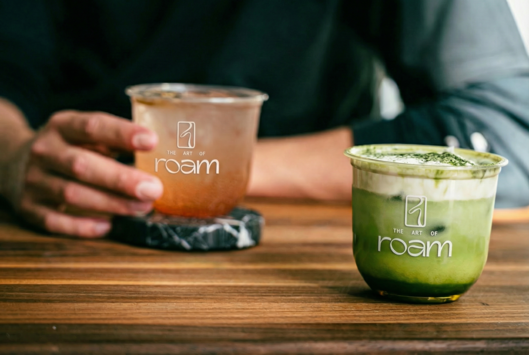 Lemonade and matcha drinks on a surface with a guest holding a cup in the background
