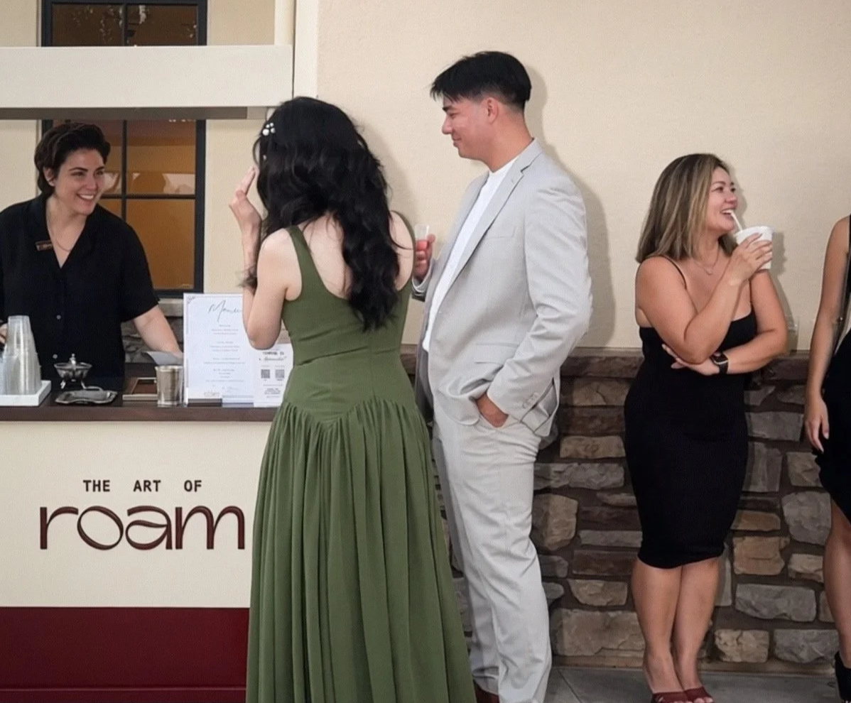 The Art of Roam barista serving coffee to wedding guests beside a cream and burgundy mobile beverage cart.