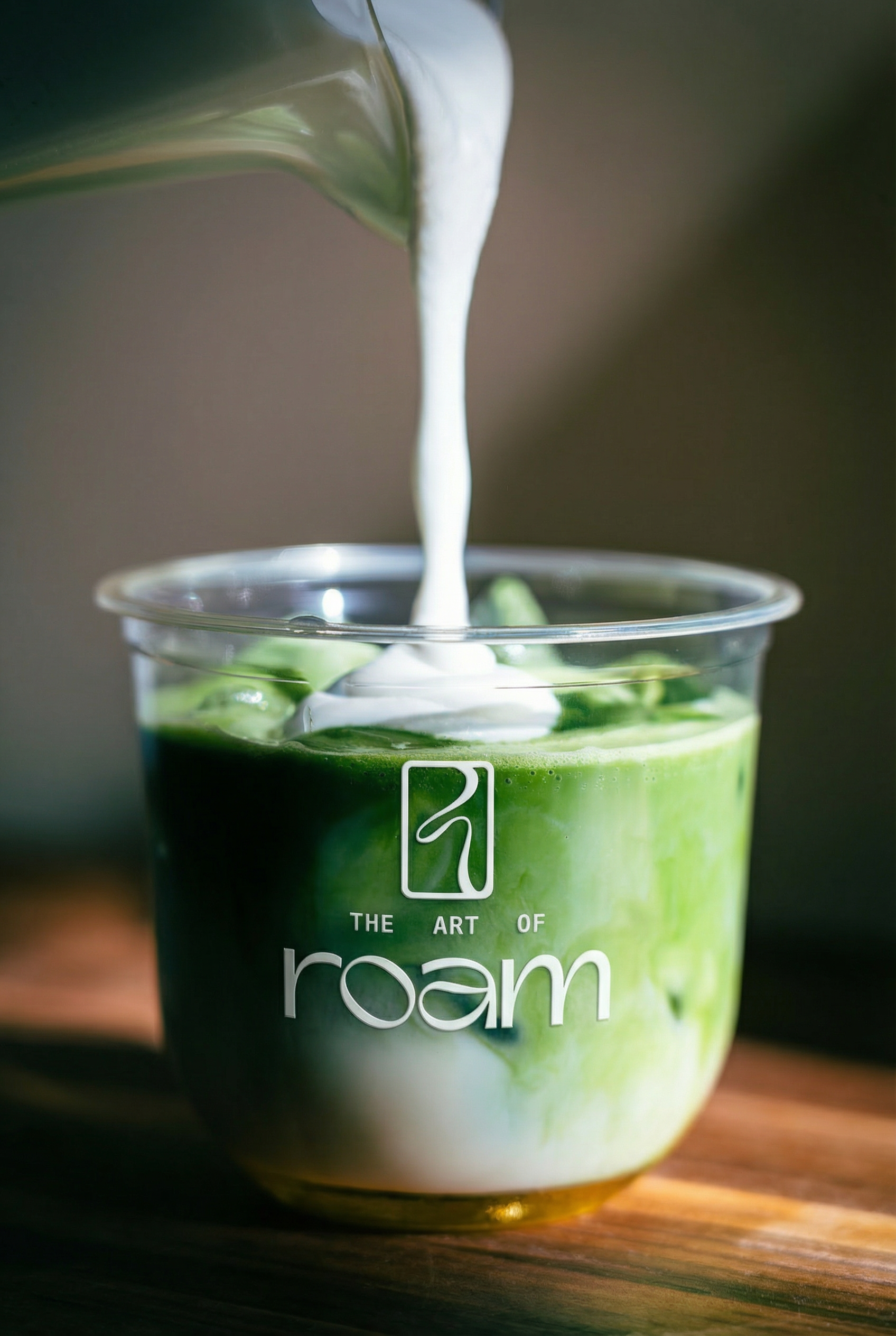 Cream being poured onto an iced matcha drink in a The Art of Roam branded cup
