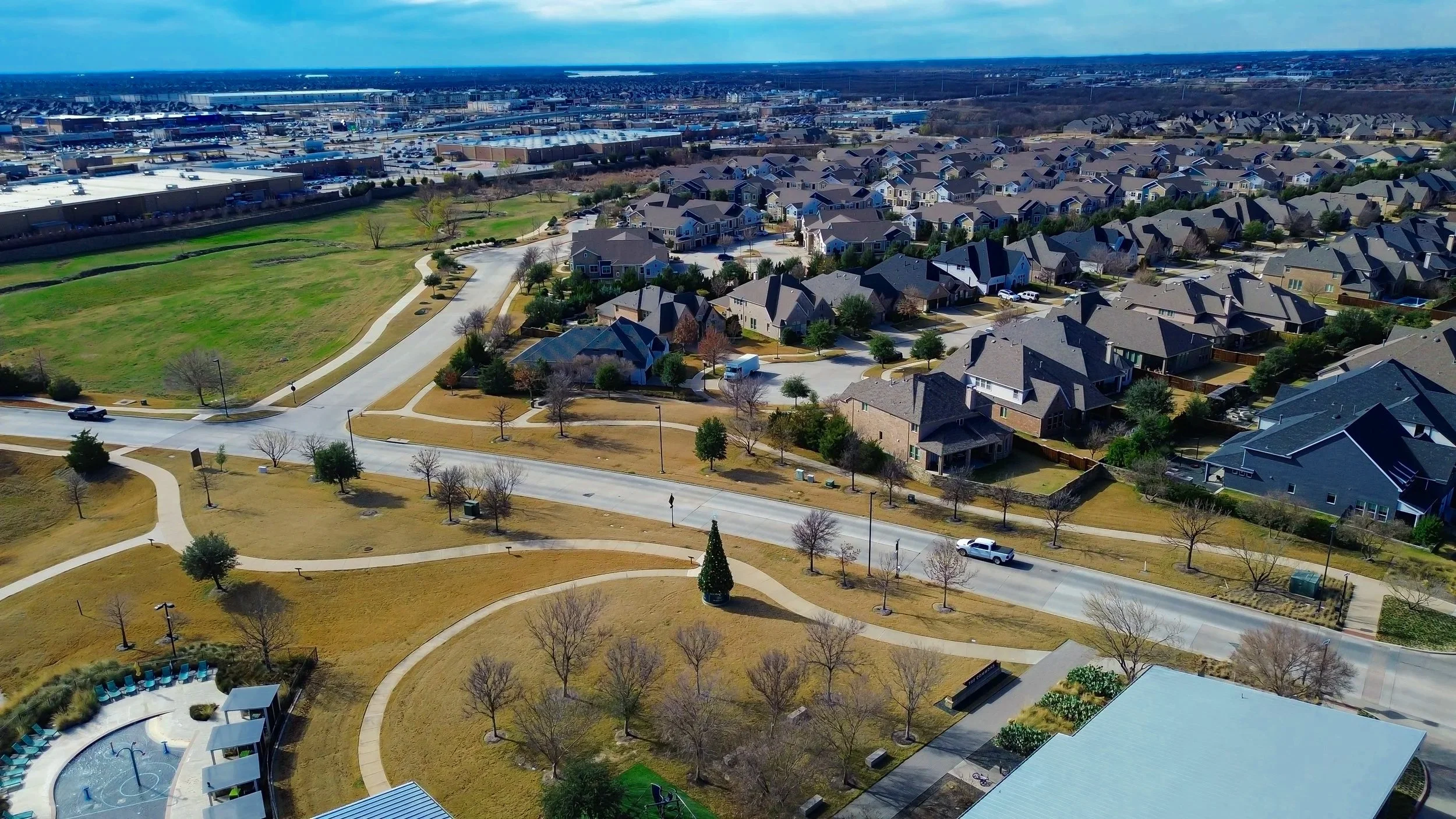 Aerial view of a suburban neighborhood with multiple houses, trees, and a park with walking paths and a small pool area.