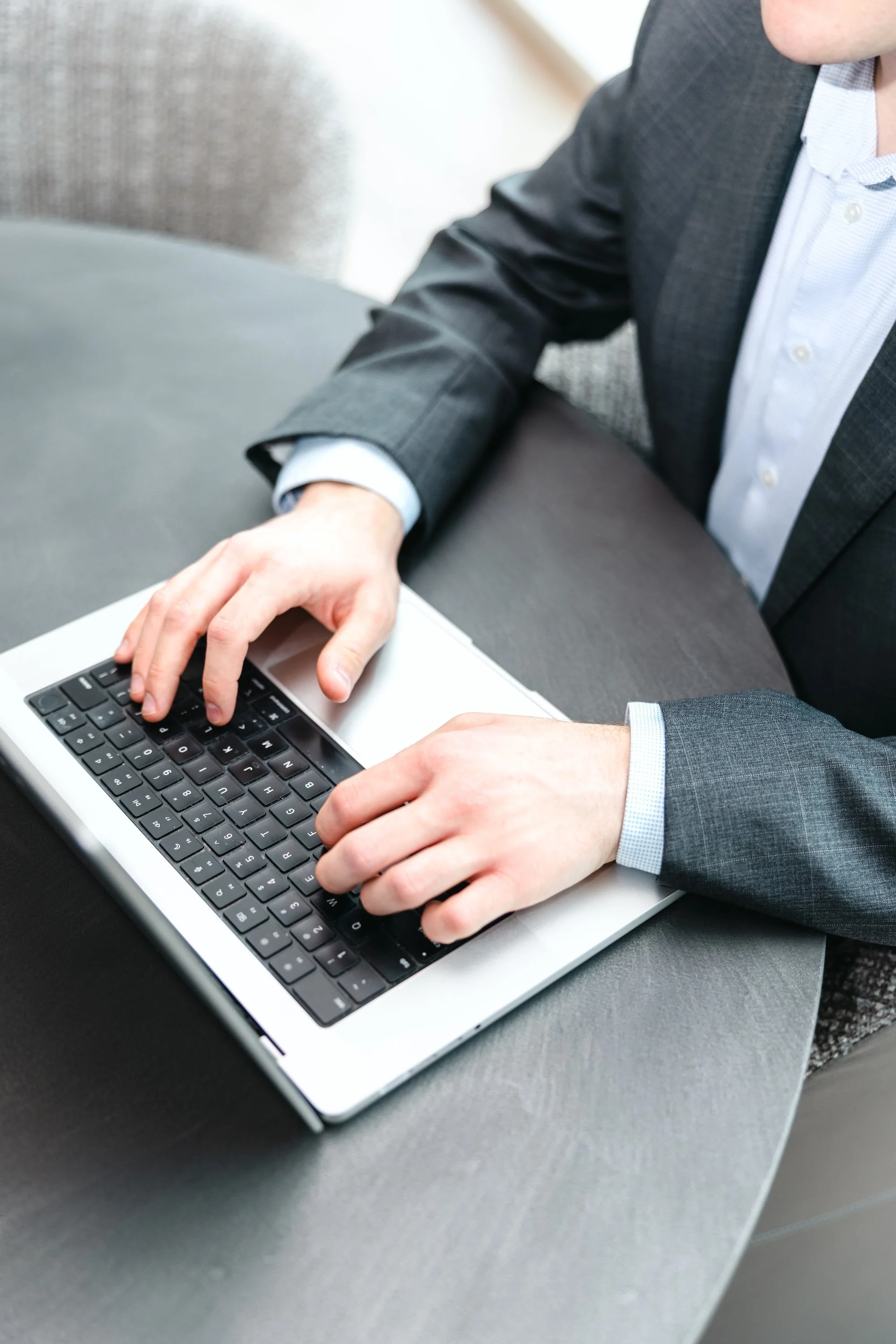 A person in a business suit typing on a laptop keyboard.
