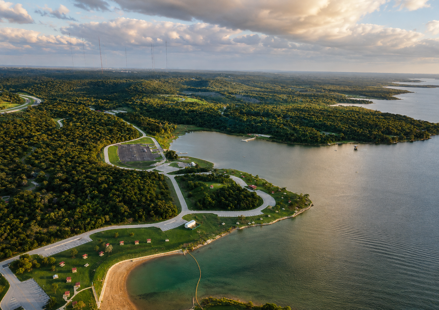 Aerial view of Cedar Hill State Park in Cedar Hill, Texas, featuring scenic lakefront shoreline, winding park roads, wooded hiking trails, and expansive North Texas landscape at sunset.