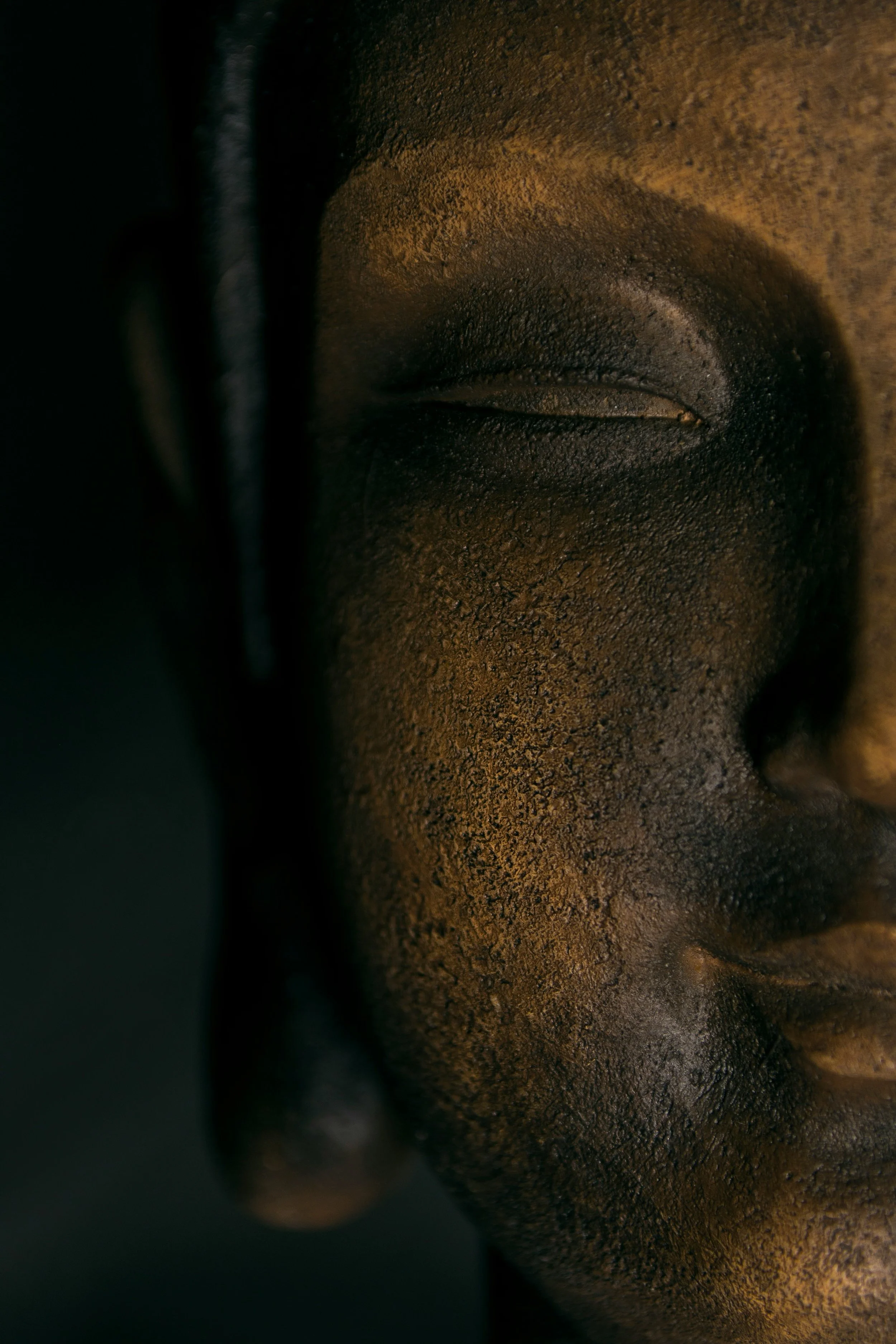 Close-up of a bronze-colored Buddha statue's face with closed eyes and textured surface representing relaxation.